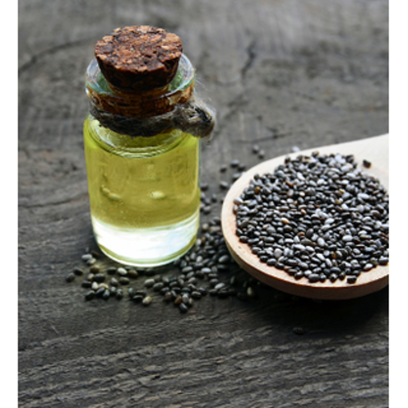 A glass bottle of Chia Seed Oil beside scattered chia seeds